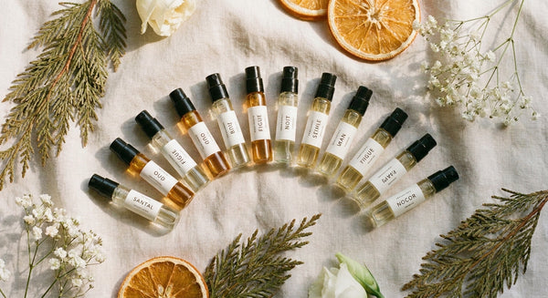 A curated collection of small perfume sample vials arranged on a light linen surface with dried botanicals in soft Nordic natural light.